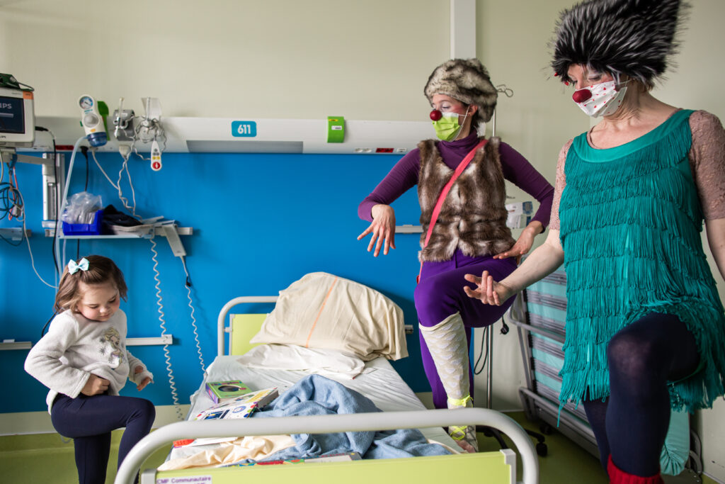 Deux clowns sont avec une jeune fille hospitalisée dans sa chambre, elles rient toutes ensemble.